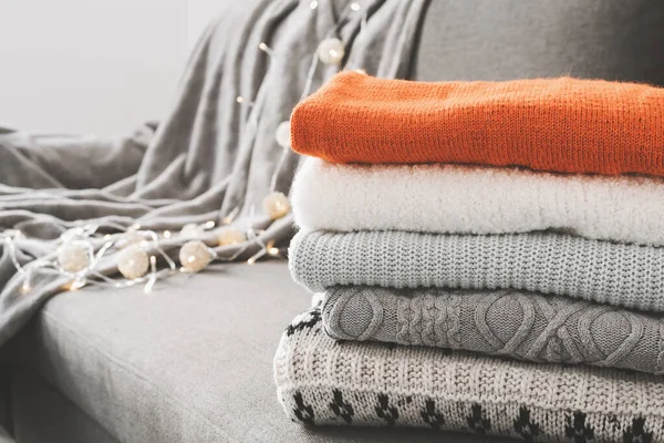 Handmade knitted sweaters on gray sofa bed. Warm clothing. Knitwear pile