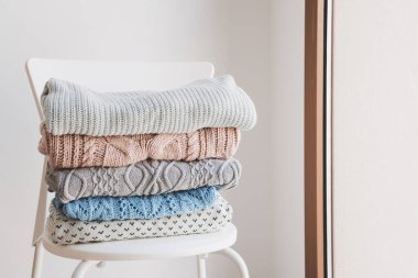 Beyaz sandalyede bir yığın sıcak kazak. Soğuk mevsim için örgü elbiseler. Asgari düzeyde. Örgü bakım konsepti