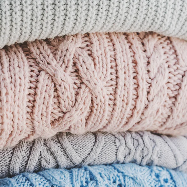 Pile of warm knitted sweaters of pastel colors. Knitwear for cold