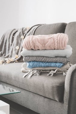 Oturma odasındaki gri kanepeye yün ve kaşmir kazaklar yığılmış. Sıcak örülmüş giysiler. El yapımı örgü bakım. 