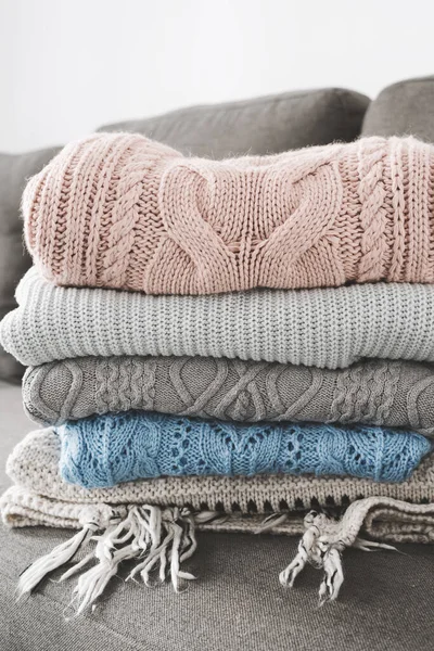 Pile of handmade knitted sweaters on gray sofa. Warm clothing. Knitwear care concept
