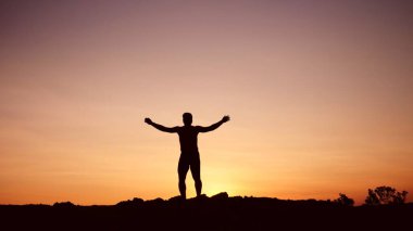 Tepede duran ve el kaldıran genç adamın silüeti.