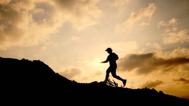 Gün batımında dağ yolunda koşan genç koşucunun silueti