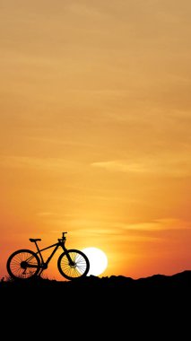 * * Bir bisiklet silueti çarpıcı turuncu bir günbatımına karşı kurulmuş, yuvarlanan tepeler huzurlu ve resimsel bir sahne yaratıyor