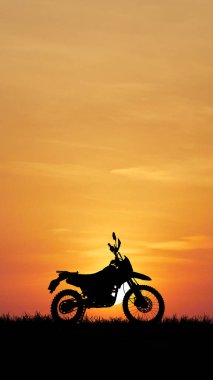 Bir motosiklet silueti çarpıcı turuncu bir gün batımına karşı duruyor, macera ve özgürlüğün özünü yakalıyor..