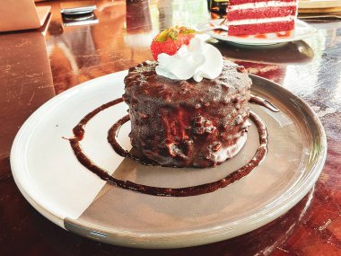 Krem şantili ve taze çilekli zengin bir çikolatalı pastanın içinde şık bir tabakta servis edilir.