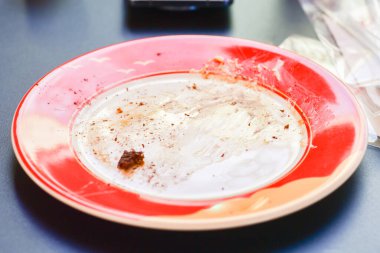 Ekmek kırıntılarıyla dolu boş bir kırmızı tabağın yakın çekimi, karanlık bir yüzeyde, yemeğin bittiğini gösteriyor..