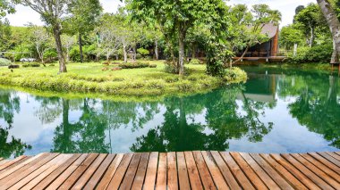 Bereketli tropikal yeşilliklerle çevrili bir göletin kenarındaki ahşap güvertenin sakin manzarası huzurlu ve huzurlu bir atmosferi yansıtıyor..
