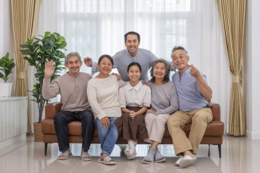 Üç kuşaktır mutlu Asyalı ailelerin portresi. Kanepenin oturma odasında toplanıp, rahat bir odada kameraya poz veriyorlar.