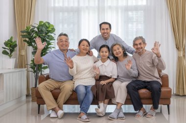 Üç kuşaktır mutlu Asyalı ailelerin portresi. Kanepenin oturma odasında toplanıp, rahat bir odada kameraya poz veriyorlar.