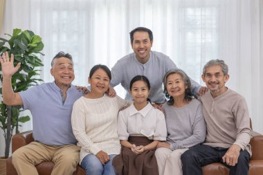 Üç kuşaktır mutlu Asyalı ailelerin portresi. Kanepenin oturma odasında toplanıp, rahat bir odada kameraya poz veriyorlar.