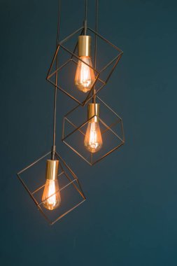 Tavandan sarkan üç kolye ışığı, geometrik tel çerçevelerin içinden koyu mavi bir duvara doğru sıcak parıltılarını gösteriyor. Bu rahat ve çağdaş bir atmosfer yaratıyor..