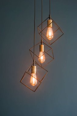 Tavandan sarkan üç şık lamba, geometrik metal çerçevelerin içinde sıcak ampuller var. Bu tasarım, odanın dekoruna çağdaş bir dokunuş ekleyerek davetkar bir atmosfer yaratıyor..