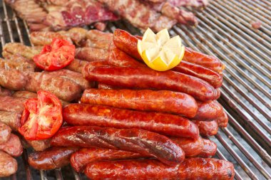 Parlak gün ışığında, çeşitli sosisler ve etler mükemmelce kızartılıyor. Taze domates ve limonlu garnitür gösteriyi güzelleştirir..