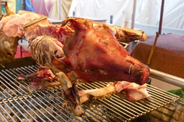 A whole pig is being grilled over an open flame at an outdoor market during a festive evening. The pig is displayed on a metal rack, waiting for hungry visitors.