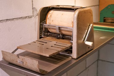 A vintage paper roller sits on a metal table in a retro workshop. The machine has a worn surface and stands against a simple wall, showcasing classic craftsmanship and nostalgia.