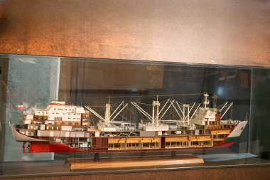 A realistic model of a cargo ship is displayed in a museum, highlighting the detailed construction and various compartments. The exhibit features modern design elements.