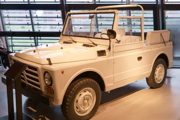 A vintage off road vehicle stands in a sleek exhibition area. The white design contrasts with the modern surroundings, showcasing its unique style and historical significance.