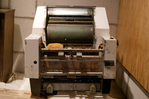 Old printing press rests in a rustic studio, highlighting its vintage design and worn features. Dust and rust suggest years of use in traditional printmaking.