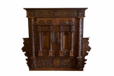 Bu ahşap dolap, kapılarında ve sütunlarında ustalık ve klasik tasarım tarzını yansıtan süslü oymalar barındırıyor. Bir mobilya parçası gibi duruyor..