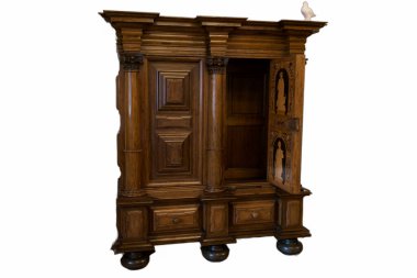 Ayrıntılı bir ahşap dolap iyi aydınlatılmış bir odada duruyor kapılarında karmaşık oymalar ve zarif bir tasarım sergiliyor. Dolabın zengin bir kapağı ve şık ayakları var. Bu da onu çarpıcı bir parça yapıyor..