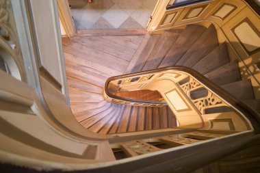 Çarpıcı ahşap bir merdiven, tarihi bir binanın içinde zarif bir şekilde esiyor. Doğal ışık, ayrıntılı korkulukları ve pürüzsüz adımları vurguluyor, keşif ve hayranlık uyandırıyor.