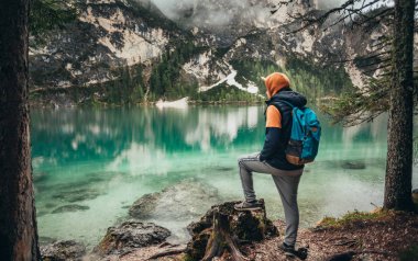 Çocuk ayna göl dağlarda, kahverengi bir ceket ve mavi bir sırt çantası içinde yürür