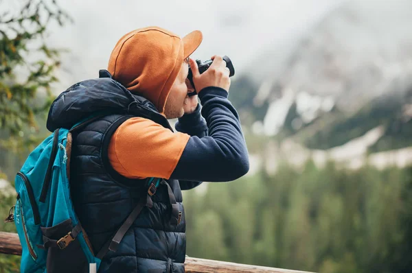 The boy walks on the mirror lake in the mountains, in a brown jacket and a blue backpack