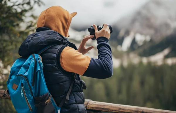 The boy walks on the mirror lake in the mountains, in a brown jacket and a blue backpack