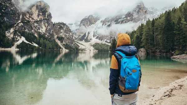Çocuk ayna göl dağlarda, kahverengi bir ceket ve mavi bir sırt çantası içinde yürür