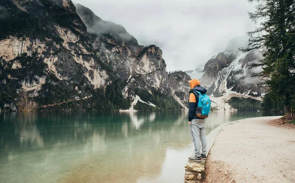 Çocuk ayna göl dağlarda, kahverengi bir ceket ve mavi bir sırt çantası içinde yürür