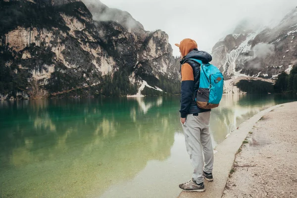 Çocuk ayna göl dağlarda, kahverengi bir ceket ve mavi bir sırt çantası içinde yürür