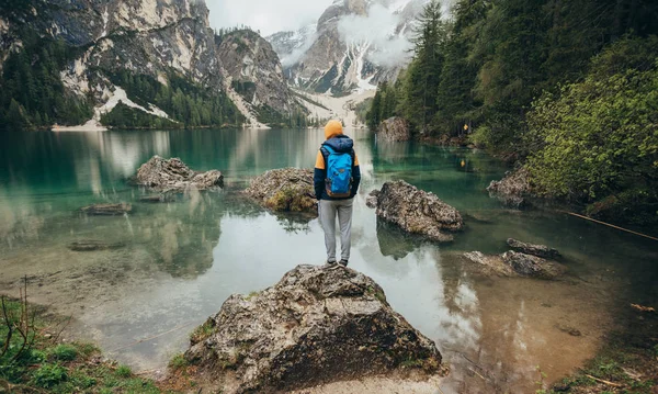 Çocuk ayna göl dağlarda, kahverengi bir ceket ve mavi bir sırt çantası içinde yürür