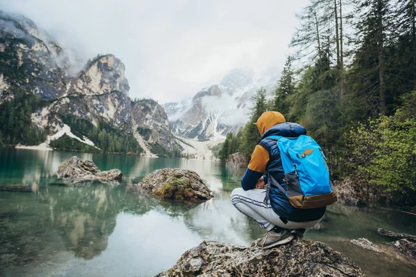 Çocuk ayna göl dağlarda, kahverengi bir ceket ve mavi bir sırt çantası içinde yürür