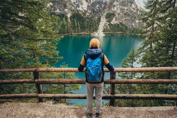 The boy walks on the mirror lake in the mountains, in a brown jacket and a blue backpack