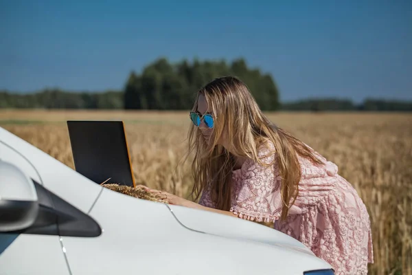 Girl working on a laptop near the field with wheat