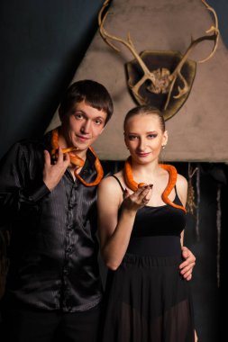 Siyah giysili güzel çift ile turuncu Mısır snakes, gülümsüyor oturur ve kameraya benziyor