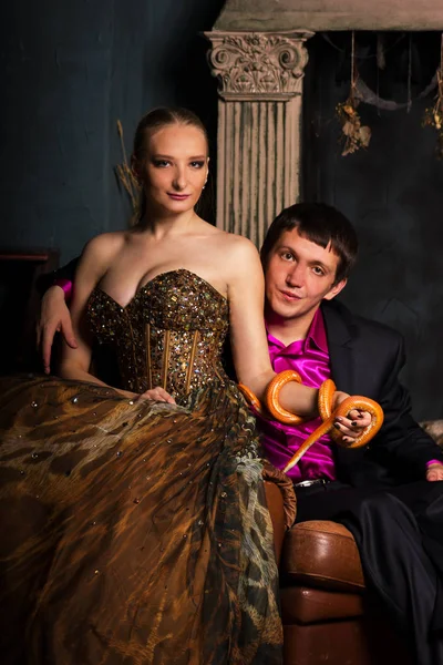 美丽的情侣在晚礼服和礼服西装坐在橙色玉米蛇 看着相机 — 图库照片