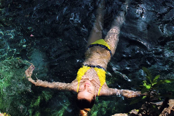 Menina bonita nova em maiô amarelo deitado na água closeup — Fotografia de Stock