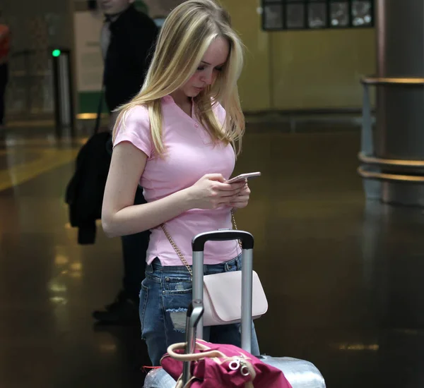 Gadis cantik muda di ruang tunggu di sebuah bangunan bandara mencari di ponsel — Stok Foto