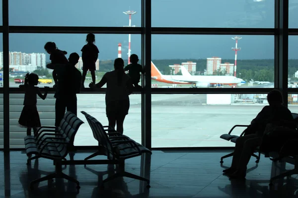 Silhouetten einer jungen Großfamilie, die am Fenster steht und mit Flugzeugen auf die Landebahn des Flughafens blickt und auf ihren Flug wartet — Stockfoto