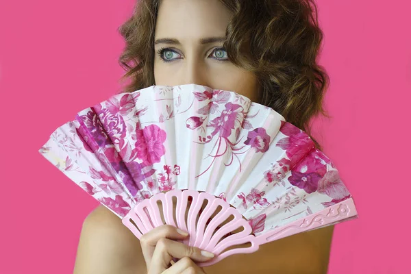 Parlak makyaj ve eller yakın çekim pembe bir arka plan üzerinde bir fan ile güzel bir genç kız portresi.