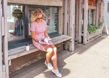 Moda haber dergi okumak ve büyük şehirde sabah kahve içme bankta oturan genç güzel sarışın kız