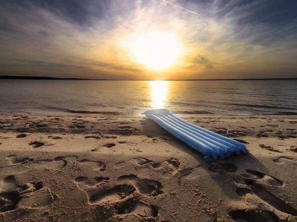 Prachtig zandstrand met voetafdrukken close-up tegen de zonsondergang in de zomer. Blauwe heldere opblaasbare matras close-up op zonsondergang achtergrond. — Stockfoto