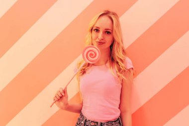 Çok renkli parlak pembe lolipop ile yumuşak pembe arka plan üzerinde pembe bir bluz genç güzel sarışın