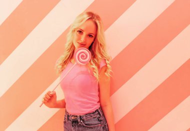 Çok renkli parlak pembe lolipop ile yumuşak pembe arka plan üzerinde pembe bir bluz genç güzel sarışın