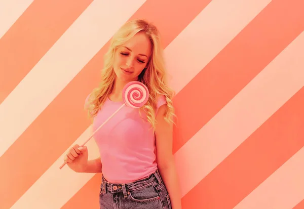 Mladá krásná blondýna v růžové halence na měkké růžové pozadí s pestrobarevným světlé růžové lízátko — Stock fotografie