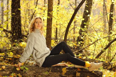 Örme kazak düşen yapraklar ile sonbahar park arka plan üzerinde genç güzel kız