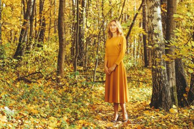 Sarı uzun elbiseli Genç güzel kız düşmüş yaprakları ile sonbahar park içeri girer.