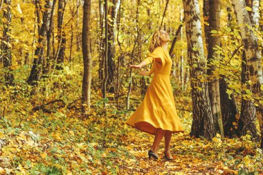 Sarı uzun elbiseli Genç güzel kız düşmüş yaprakları ile sonbahar park içeri girer.